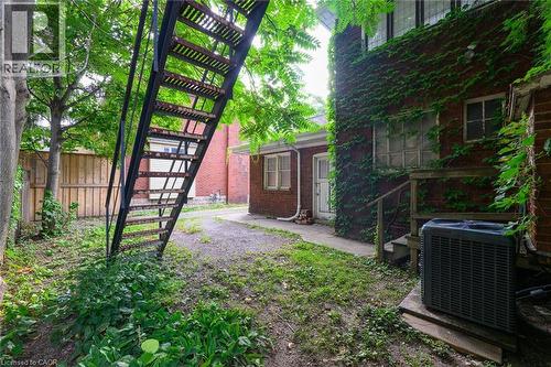 Brick exterior with climbing vines, exterior metal staircase, mature trees, and a wooden privacy fence - 414 Main Street E, Hamilton, ON 