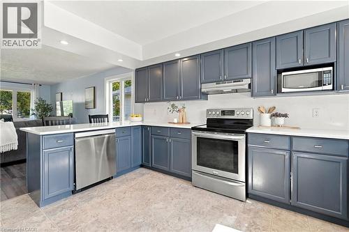 Kitchen featuring blue shaker-style cabinetry, stainless steel appliances, white countertops, and tile flooring - 915 St George Street, Port Dover, ON 