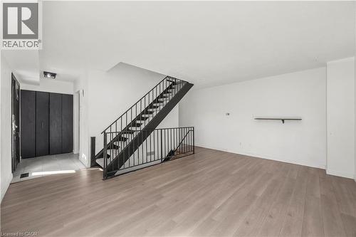 Expansive room with wood-finish flooring, white walls, and a black metal staircase - 70 Fiddlers Green Road Unit# 74, London, ON 