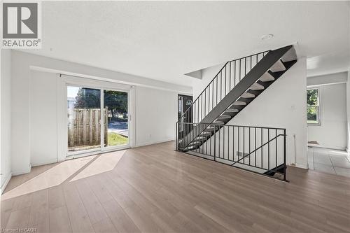 Spacious living area featuring wood-finish flooring, a contemporary staircase with metal railings, a sliding glass door, and white painted walls - 70 Fiddlers Green Road Unit# 74, London, ON 