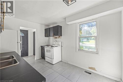 Kitchen featuring upper and lower cabinetry, a double basin sink, electric range, and tile flooring - 70 Fiddlers Green Road Unit# 74, London, ON 