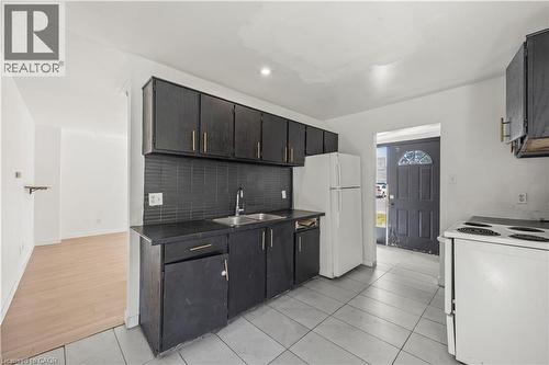 Kitchen featuring dark cabinetry, a coordinating dark backsplash, a stainless steel sink, and tile flooring - 70 Fiddlers Green Road Unit# 74, London, ON 