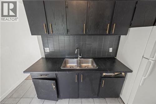 Black cabinetry with gold-finish hardware, black subway tile backsplash, and a double basin stainless steel sink - 70 Fiddlers Green Road Unit# 74, London, ON 
