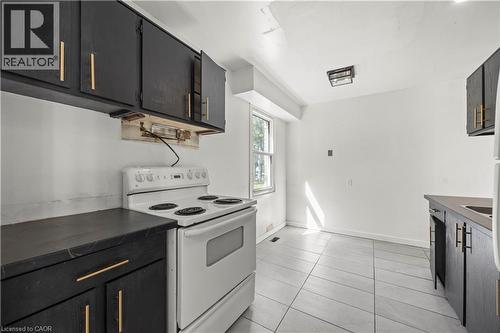 Kitchen featuring black cabinetry with gold-toned hardware, white electric range, and tiled flooring - 70 Fiddlers Green Road Unit# 74, London, ON 