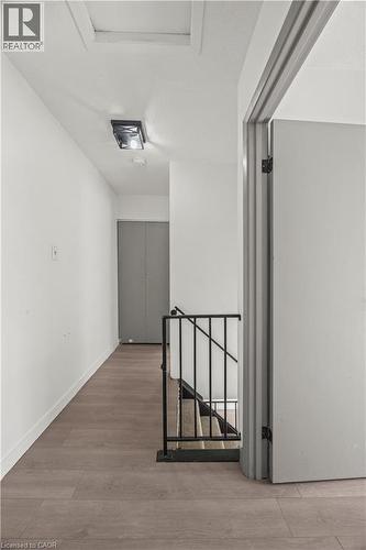 Hallway with wood-finish flooring, white walls, and a black wrought iron stair railing - 70 Fiddlers Green Road Unit# 74, London, ON 