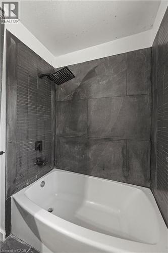 White drop-in bathtub with dark stone-finish wall tile and a square rain showerhead - 70 Fiddlers Green Road Unit# 74, London, ON 