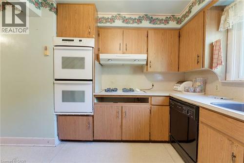 Built-in double oven, wood-finish cabinetry, integrated dishwasher, and a gas cooktop - 940 Harvey Place, Halton, ON 