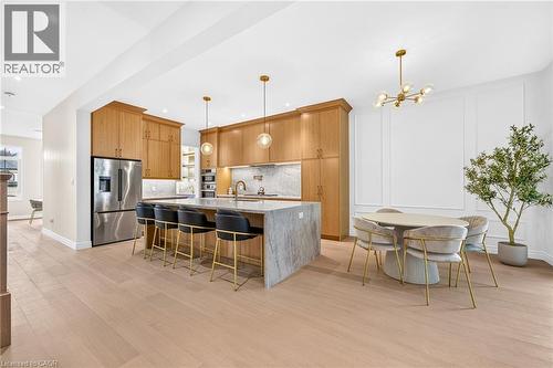 Open-concept kitchen and dining area featuring light wood-finish flooring, full-height cabinetry, a large kitchen island with counter seating, stainless steel appliances, and a decorative wall panel - 67 Cielo Court, Hamilton, ON 