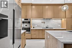 Light wood cabinetry with integrated stainless steel appliances, a pot filler, under-cabinet lighting, and stone countertops - 