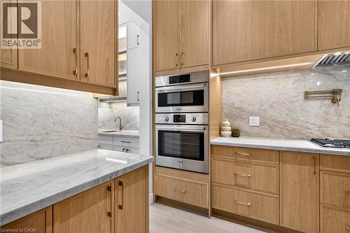 Wood-finish cabinetry, light-toned stone countertops, integrated stainless steel appliances, stone backsplash, and recessed under-cabinet lighting - 67 Cielo Court, Hamilton, ON 