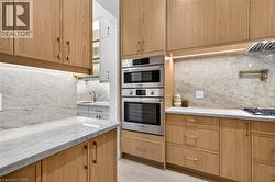Wood-finish cabinetry, light-toned stone countertops, integrated stainless steel appliances, stone backsplash, and recessed under-cabinet lighting - 