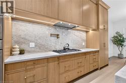 Custom light wood-finish cabinetry, solid surface countertops, patterned backsplash, built-in gas range, and a pot filler - 