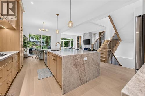 Hardwood flooring throughout, kitchen island with stone countertop, wood cabinetry with gold-tone hardware, built-in stainless steel appliances, and a staircase with wood and metal railings - 67 Cielo Court, Hamilton, ON 