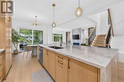Spacious kitchen island with a stone countertop, light wood-finish cabinetry, and contemporary pendant lighting - 