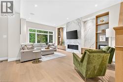 Spacious living area featuring expansive windows, wood-finish flooring, a wall-mounted fireplace, and built-in shelving - 