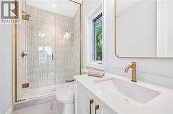Walk-in shower with clear glass enclosure and gold-toned fixtures, rectangular wall-mounted mirror, single vanity with integrated sink, gold-toned faucet, and white countertop - 