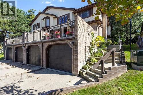 Multi-level residence featuring brick and siding exterior, multiple garage bays, a second-story balcony with metal railings, and exterior wooden stairs leading to the upper entry - 475 Beechwood Drive Unit# 4, Waterloo, ON 