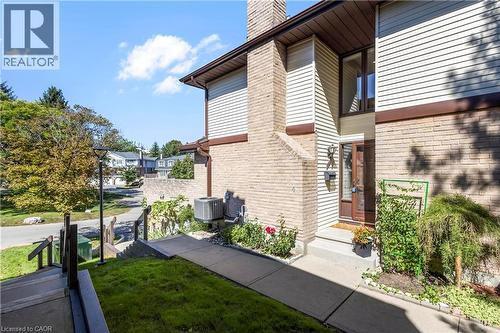 Brick and siding exterior with a prominent chimney, concrete walkway, and landscaped garden beds - 475 Beechwood Drive Unit# 4, Waterloo, ON 