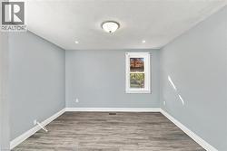 Interior room featuring light-toned walls, wood-finish flooring, a single-pane window with white trim, and a ceiling-mounted dome light fixture - 