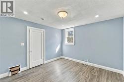 Neutral-toned room featuring wood-finish flooring, a single-panel interior door, recessed lighting, and a flush-mount ceiling fixture - 