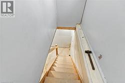 Staircase featuring unfinished wood treads and a wood handrail with drywall-surrounded wall surfaces - 