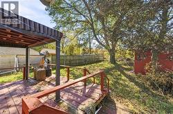Elevated wood deck featuring a covered pergola, red-stained wooden railing, and an expansive backyard with mature trees and perimeter fencing - 