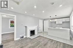 Open-concept space featuring a white decorative mantel fireplace, wood-finish flooring, a kitchen island with a white countertop, high-gloss white cabinetry, and recessed lighting - 