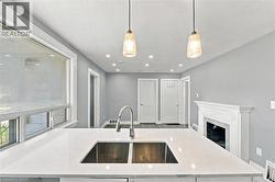 Kitchen island featuring a stone countertop with an undermount double-basin stainless steel sink and a high-arc faucet, complemented by dual pendant lights, recessed ceiling lighting, and a fireplace - 