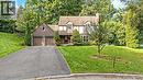 Tudor-style exterior with a shingled roof, attached two-car garage, expansive front lawn, and mature trees - 12 Mullen Place, Glen Williams, ON 