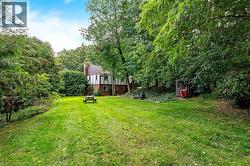 Expansive lawn bordered by mature trees, featuring a Tudor-style residence with brick and stucco facade, and a prominent chimney - 