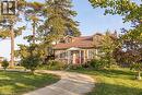 Stone facade residence featuring a metal roof, dormer windows, a covered front porch, and mature trees surrounding the property - 2744 Bleams Road, New Hamburg, ON 