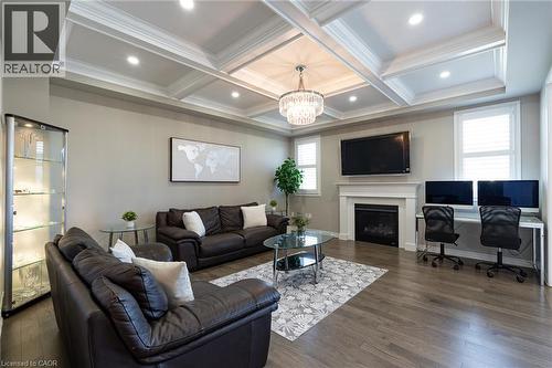 Coffered ceiling with recessed lighting and a chandelier, wood-finish flooring, white fireplace with mantle, and window shutters - 455 Equestrian Way, Cambridge, ON 