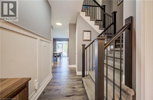 Wood-finish flooring throughout the hallway, wainscoting detail on the wall, and a staircase with metal balusters and carpeted treads - 35 Greyhawk Street, Kitchener, ON 