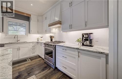 White shaker-style cabinetry with ample storage, polished granite countertops, white subway tile backsplash, stainless steel range, and wood-finish flooring - 35 Greyhawk Street, Kitchener, ON 