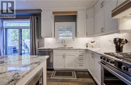 White cabinetry with contrasting hardware, light-toned countertops, subway tile backsplash, stainless steel appliances, and wood-finish flooring - 35 Greyhawk Street, Kitchener, ON 
