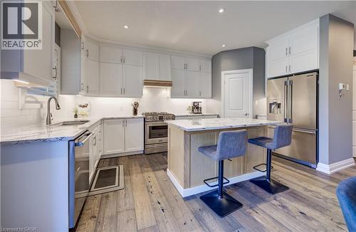 Kitchen featuring white cabinetry, stainless steel appliances, wood-finish flooring, a central island with a stone countertop, and recessed lighting - 35 Greyhawk Street, Kitchener, ON 