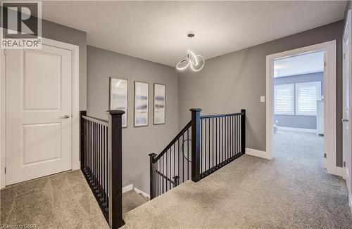 Upper-level landing featuring textured carpeting, neutral wall colors, contemporary ceiling fixture, and dark wood newel posts with iron balusters - 35 Greyhawk Street, Kitchener, ON 