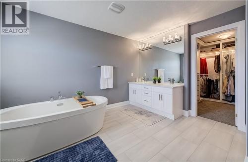 Freestanding soaking tub, double vanity with white cabinetry, light gray tile flooring, and integrated walk-in closet with built-in shelving - 35 Greyhawk Street, Kitchener, ON 