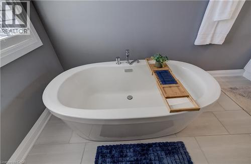 Freestanding soaking tub with chrome fixtures, set against a window with white plantation shutters and light-toned tile flooring - 35 Greyhawk Street, Kitchener, ON 