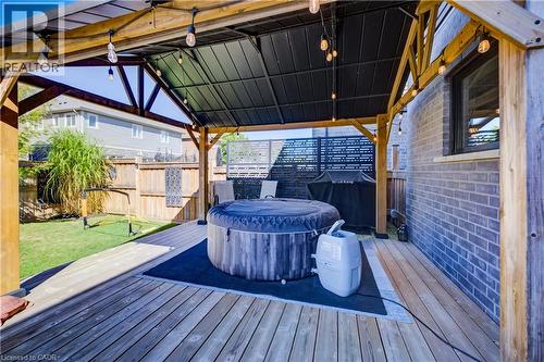 Expansive wood deck with a built-in pergola featuring string lighting, complemented by a manicured lawn and a brick exterior wall - 35 Greyhawk Street, Kitchener, ON 