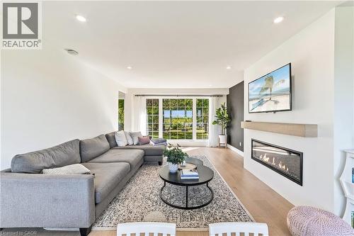 Recessed lighting illuminating the room, wood-finish flooring, large multi-pane windows, built-in linear fireplace with a wood mantle, and a contrasting accent wall - 5367 2 Side Road, Milton, ON 