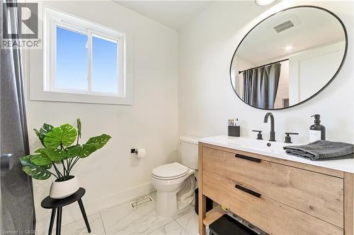 Vanity with wood-finish cabinetry, white countertop, matte black fixtures, and an oval mirror - 5367 2 Side Road, Milton, ON 