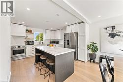 Bright kitchen with wood-finish flooring, white cabinetry, a central island with a light-toned countertop, and stainless steel appliances - 