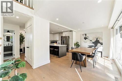 Open-concept main level featuring wood-finish flooring, a modern kitchen island with seating, recessed lighting, and a powder room with a vanity and round mirror - 5367 2 Side Road, Milton, ON 