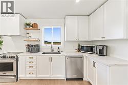 White shaker cabinetry, light-toned wood-finish flooring, stainless steel appliances, a stainless steel sink, and light-toned countertops - 
