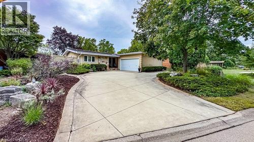 Stone façade residence with an attached garage, featuring a concrete driveway, established trees, and natural landscaping - 89 Little John Road, Dundas, ON 