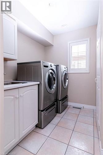 Laundry area featuring ceramic tile flooring, built-in cabinetry, a utility sink, and a window with white shutters - 89 Little John Road, Dundas, ON 