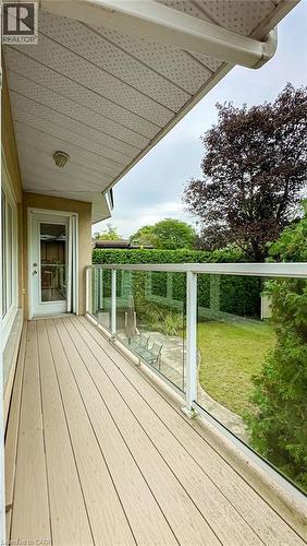 Covered exterior balcony featuring composite decking, clear glass railing, and a rear yard with mature perimeter landscaping - 89 Little John Road, Dundas, ON 
