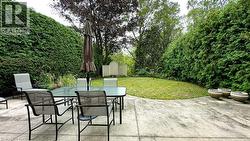 Paved patio with a curved lawn area and substantial perimeter hedges - 