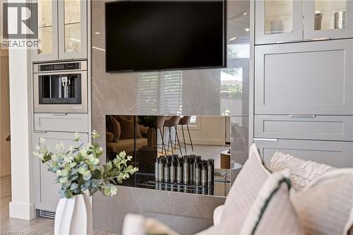 Built-in coffee system, custom cabinetry with glass-front uppers, integrated wall-mounted television, and a decorative fireplace with a reflective surround - 5056 New Street Unit# 4, Burlington, ON 